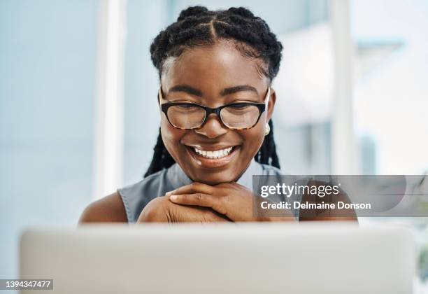 happy african businesswoman wearing glasses and working on a laptop in an office alone - happy face glasses stockfoto's en -beelden