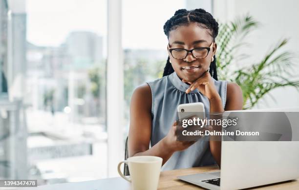 young black businesswoman using a cellphone while working on a laptop in an office alone - notificatiepictogram stockfoto's en -beelden