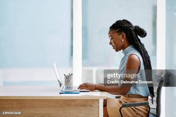 junge schwarze geschäftsfrau, die allein in einem büro an einem laptop arbeitet - african woman happy stock-fotos und bilder