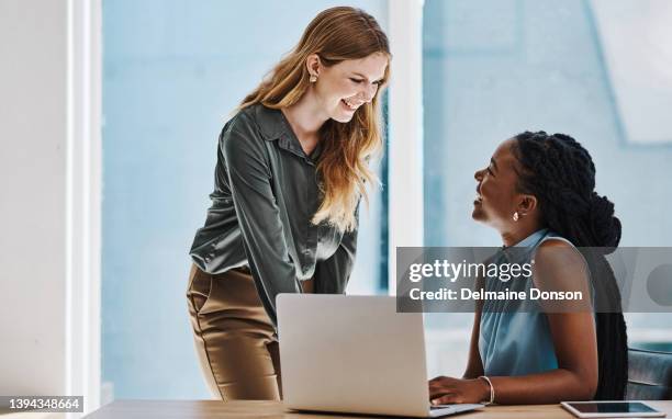 two confident young businesswomen having a discussion while working together on a laptop in an office - straff stock pictures, royalty-free photos & images