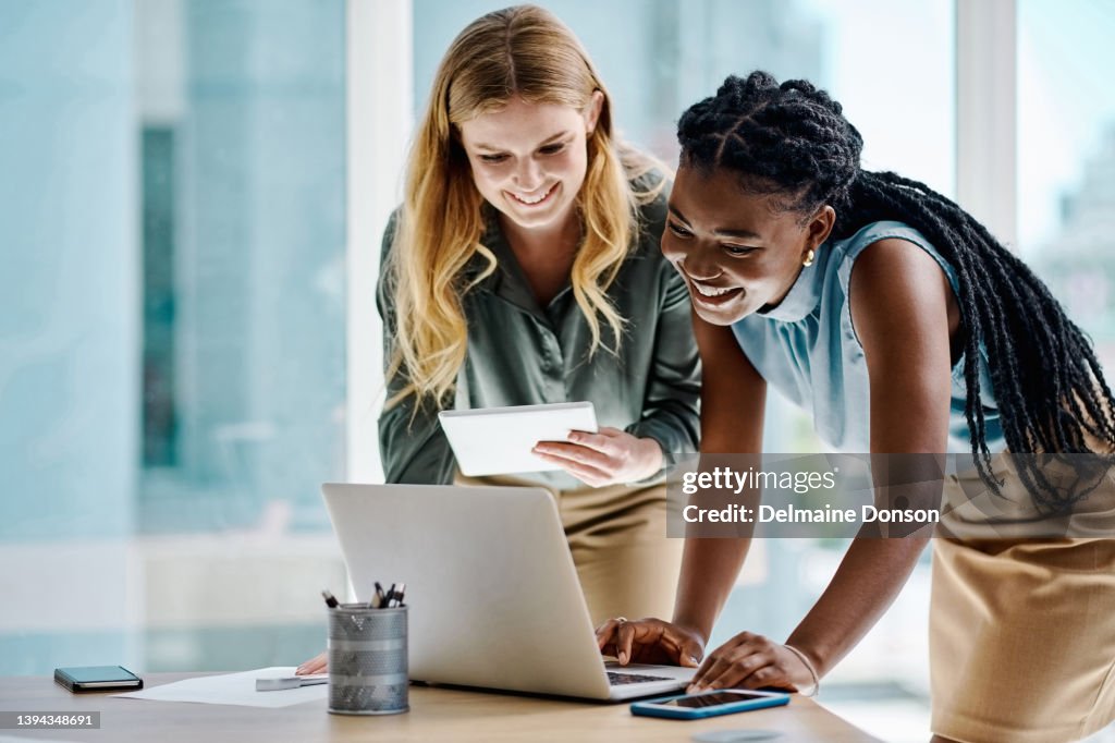 Zwei unterschiedliche Geschäftsfrauen, die gemeinsam an einem digitalen Tablet und Laptop in einem Büro arbeiten