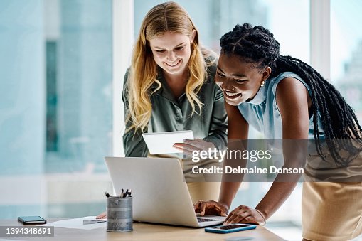 Two diverse businesswomen working together on a digital tablet and laptop in an office Two diverse businesswomen working together on a digital tablet and laptop in an office