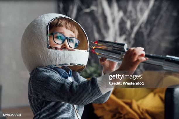 boy wearing space helmet playing with toy rocket at home - astronaut kid stockfoto's en -beelden