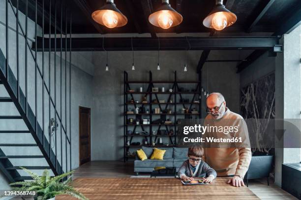 boy turning pendant lights on through tablet pc sitting by grandfather at home - pendant light stockfoto's en -beelden