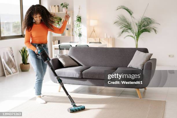 smiling young woman with vacuum cleaner dancing in living room at home - vacuum cleaner woman stockfoto's en -beelden