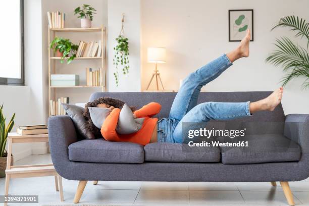 young woman hugging pillow lying on sofa in living room at home - moving sofa stock pictures, royalty-free photos & images