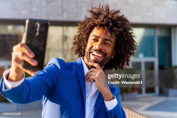 happy businessman with hand on chin taking selfie through mobile phone in front of building - selfie male stock pictures, royalty-free photos & images
