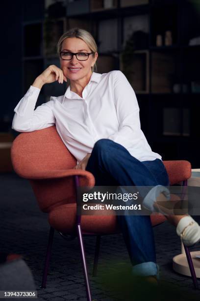 smiling businesswoman with head in hand sitting on chair - donna poltrona foto e immagini stock