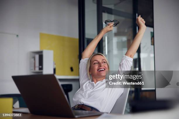 Happy Businesswoman Stretching With Arms Raised In Office High-Res Stock Photo