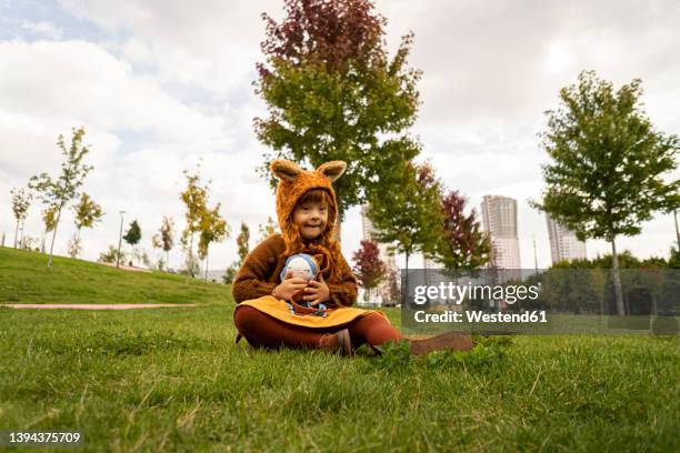 girl with down syndrome sitting on grass in public park - bear suit 個照片及圖片檔