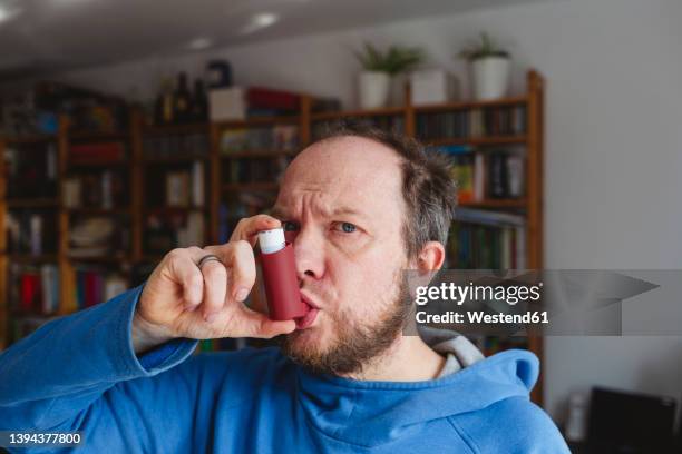 man using asthma inhaler at home - asthmainhalator stock-fotos und bilder