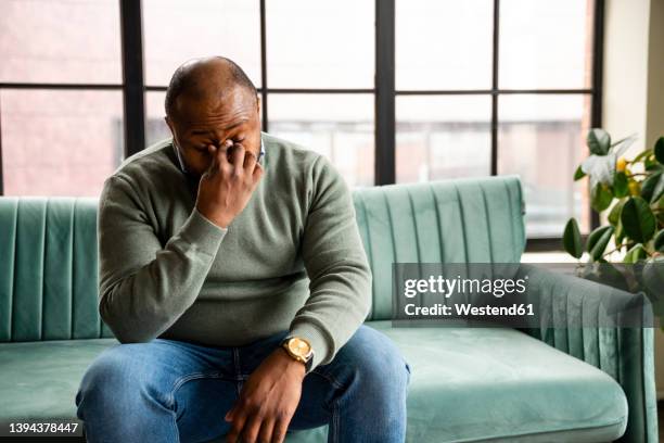 exhausted businessman rubbing eyes sitting on sofa in office - frotarse los ojos fotografías e imágenes de stock