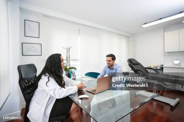 dermatologist discussing with patient sitting at desk in aesthetic clinic - dermatologists talking to each other patient stock pictures, royalty-free photos & images