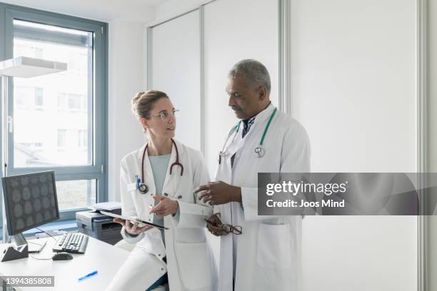 two doctors discussing medical test results using digital tablet - two doctors talking stockfoto's en -beelden