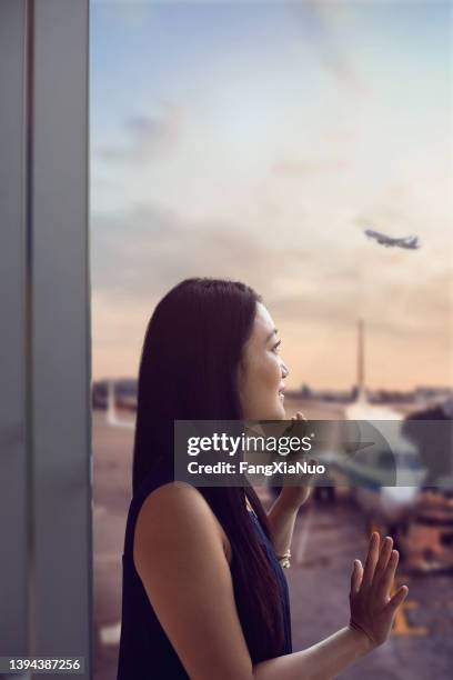 young chinese woman standing at airport terminal departure area waving to airplane - launch of i believe you project stock pictures, royalty-free photos & images