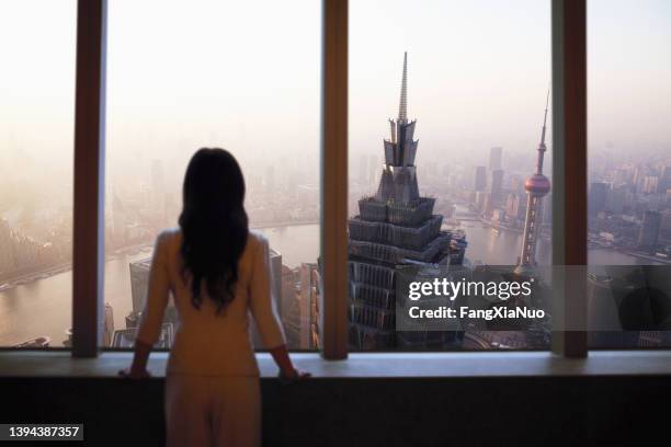 jovem de terno olha para o horizonte de xangai de janela em prédio - shanghai world financial center - fotografias e filmes do acervo