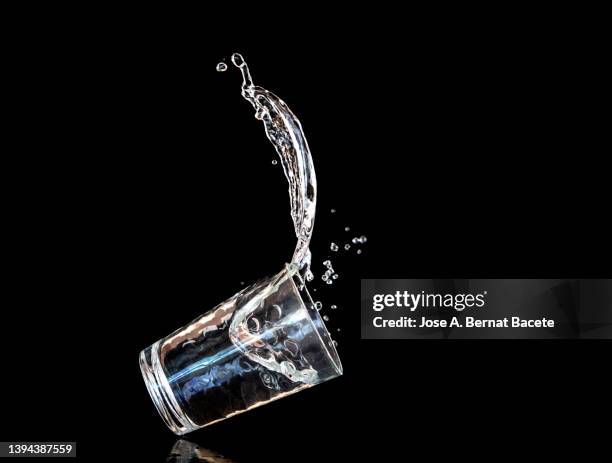 a crystal glass of water falls to the ground on a black background. - chorro agua fotografías e imágenes de stock