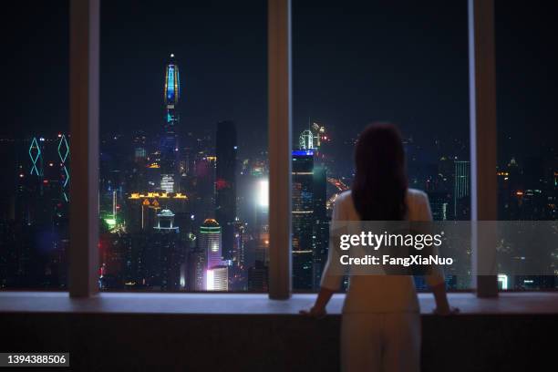 young woman in suit looks at shenzhen skyline from window in building - night before stock pictures, royalty-free photos & images