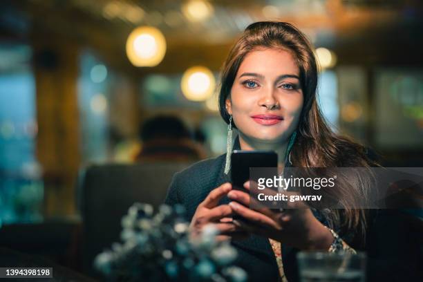 businesswoman relaxes and uses a smartphone in a restaurant. - drop earring stock pictures, royalty-free photos & images