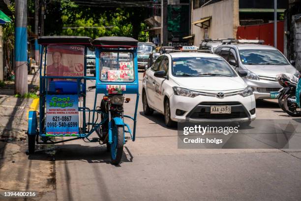makati metro manila street scene with taxi passing a parked tricycle - philippines tricycle stock pictures, royalty-free photos & images