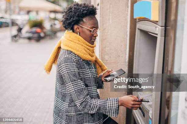 young black women talking on the mobile phone and  using atm and taking cash from the card - atm cash stock pictures, royalty-free photos & images