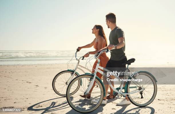 two people young caucasian couple enjoying riding bicycles on holiday at the beach - bike beach stockfoto's en -beelden