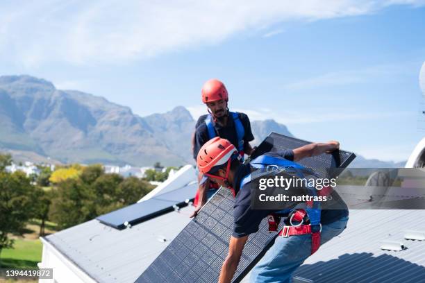 arbeiter heben und installieren sonnenkollektoren auf dem dach eines hauses - lift roof stock-fotos und bilder