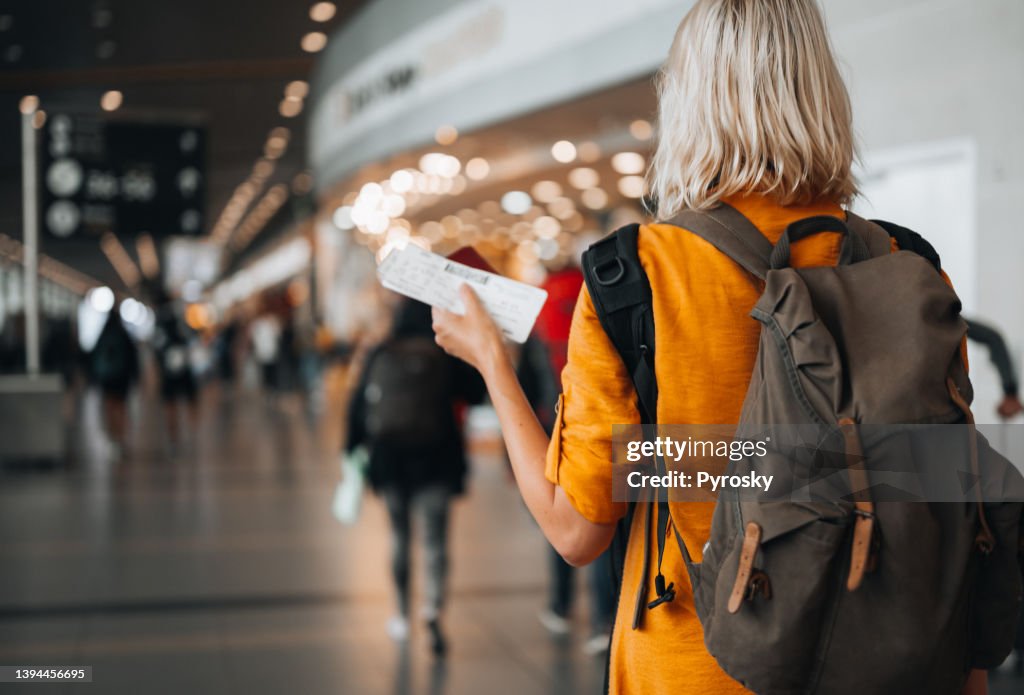 A woman at the airport holding a passport with a boarding pass