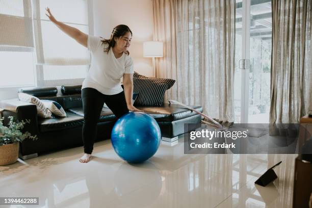 glückliches asiatisches plus-size-mädchen, das eine kurze und einfache übung mit ball in ihrem wohnzimmer macht. - chubby asian girl stock-fotos und bilder