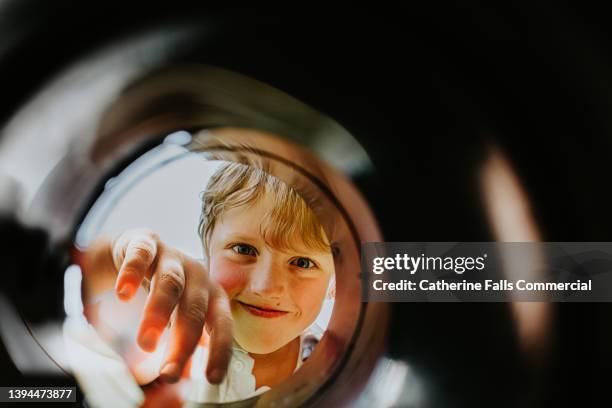 a cute young boy looks into a container with curiosity, and smiles as he reaches inside - bambino curioso foto e immagini stock