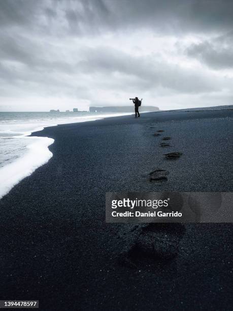 footprints in the ash sand leading to a professional photographer on an icelandic beach - photographer seascape stock pictures, royalty-free photos & images