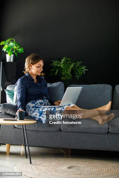 woman relaxing on the sofa after work, using laptop and enjoying coffer - navy blue living room stock pictures, royalty-free photos & images