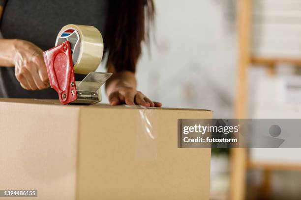 femme d’affaires debout au-dessus de son bureau, scotchant une boîte avec du ruban adhésif - tape dispenser photos et images de collection