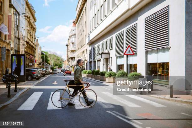 commuter pushing his bicycle on the crosswalk - pedestrian crossing man stock pictures, royalty-free photos & images