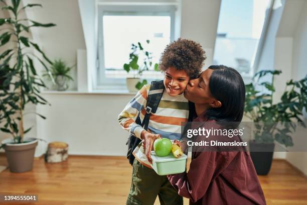 mother kissing her son who is going to school - schoolbag lunchbox lunch stockfoto's en -beelden