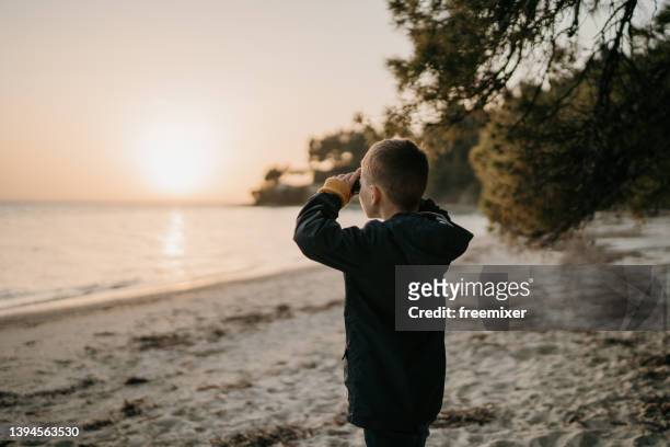 neugieriges kind, das durch ein fernglas am strand schaut - boy exploring on beach stock-fotos und bilder