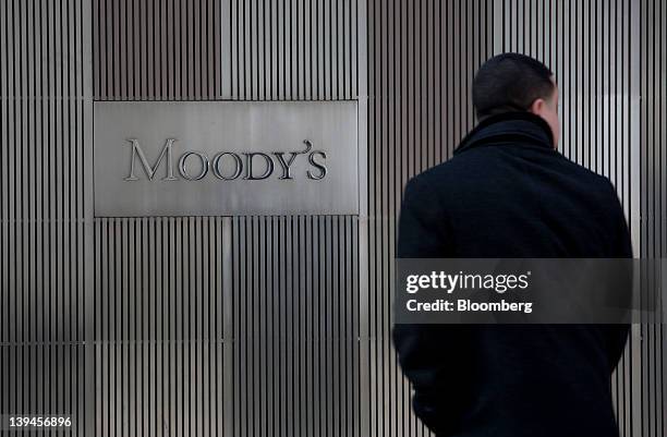 Pedestrians walk past the Moody's Investors Service Inc. Logo displayed outside of the company's headquarters in New York, U.S., on Tuesday, Feb. 21,...