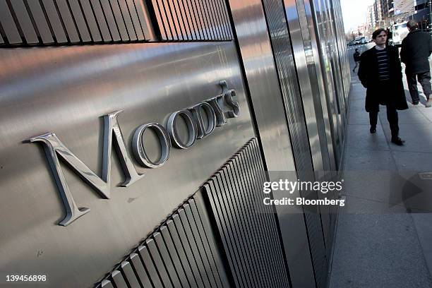 Pedestrians walk past the Moody's Investors Service Inc. Logo displayed outside of the company's headquarters in New York, U.S., on Tuesday, Feb. 21,...
