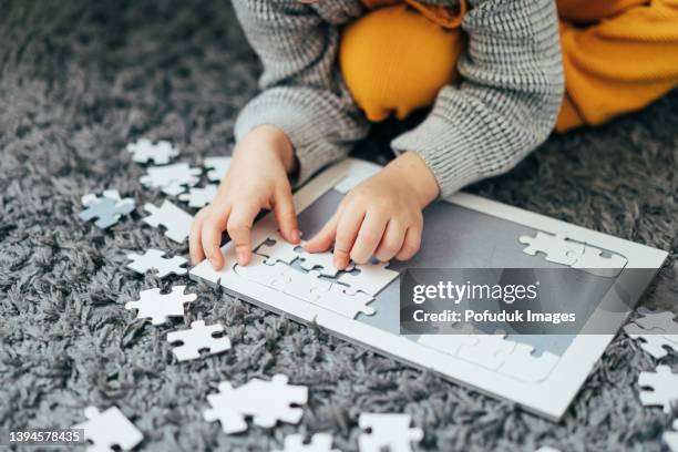 garçon mignon faisant un puzzle sur un tapis - jigsaw piece stock photos et images de collection