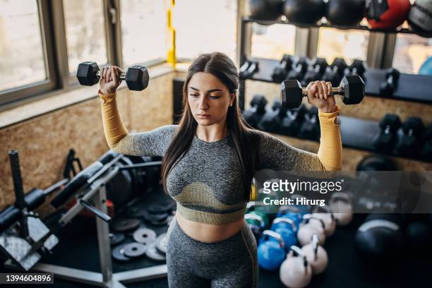 young woman training with dumbbells - women's weightlifting stock pictures, royalty-free photos & images