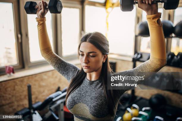 giovane donna che si allena con manubri - sollevamento pesi femminile foto e immagini stock