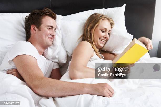 couple giggle in bed as man approaches woman from behind as she reads a book at bedtime, hoping for some nookie - woman reaching hands towards camera stock pictures, royalty-free photos & images