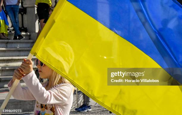 Little girl waves the Ukrainian flag as Ukrainian residents in Portugal display their country's national colors while answering to Ukrainian Refugees...