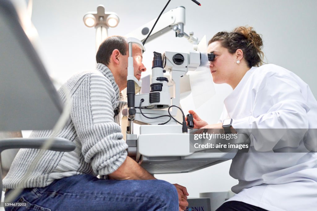 Female ophthalmologist examining male patient in ophthalmology clinic with autorefractometer, examination of eyesight.