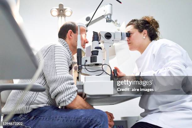 female ophthalmologist examining male patient in ophthalmology clinic with autorefractometer, examination of eyesight. - visão saúde e medicina - fotografias e filmes do acervo