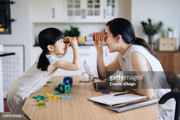 young asian mother working from home on laptop while little daughter playing with her on the desk. they are enjoying the time together at home. home office and business concept. working mom managing work life and home life - asian mum stockfoto's en -beelden