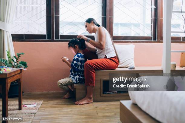 adorable little asian girl playing a game on a smartphone while her mother ties her hair - family wide angle stock pictures, royalty-free photos & images