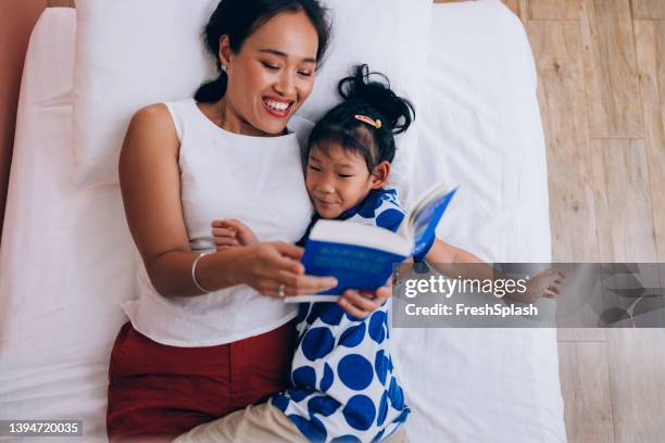 happy thai mother lying on the bed with her cute little daughter and reading her a story before an afternoon nap - bed overhead view stock pictures, royalty-free photos & images