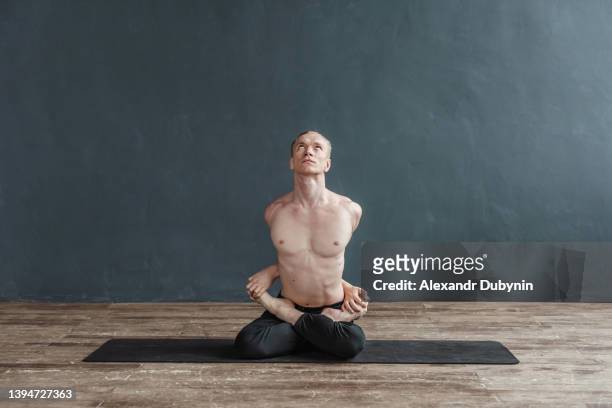 flexible male yogi practices yoga while sitting on a mat on the floor in a yoga class. the person meditates in a pose for stretching and relaxation. the man is a master of meditation - yogi stock pictures, royalty-free photos & images