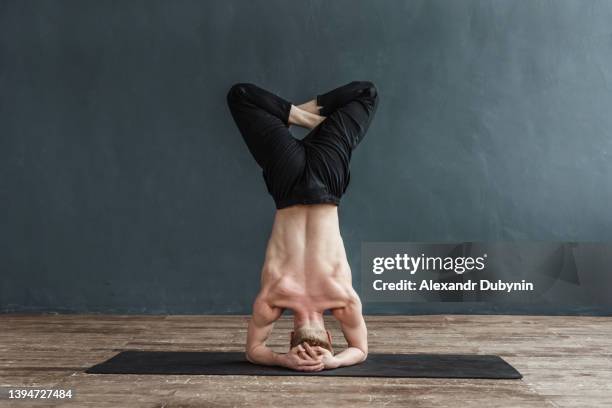 yogi man doing yoga exercise on mat while standing on his head. flexible male headstand in lotus position stretching training. - yogi stock-fotos und bilder